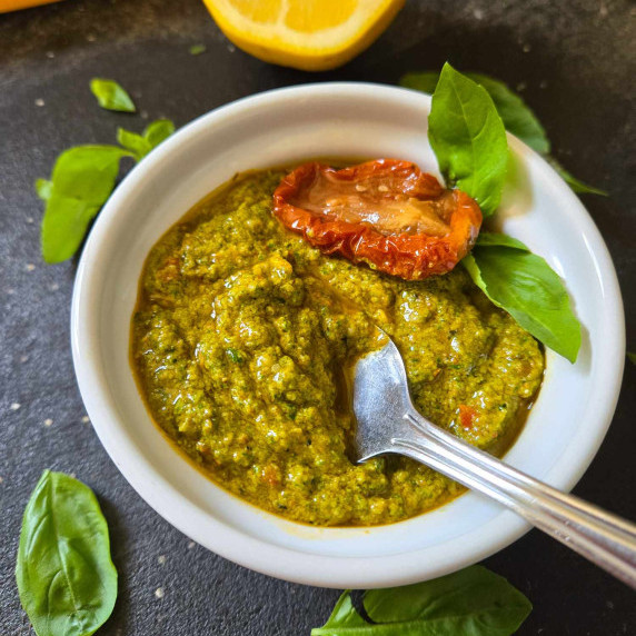 A gorgeous and fresh, vibrant pesto in a white bowl against a black cutting board.