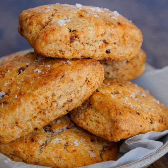 Reddish sundried tomato and cheese scones in a bowl stacked up tall with flaky salt on top.