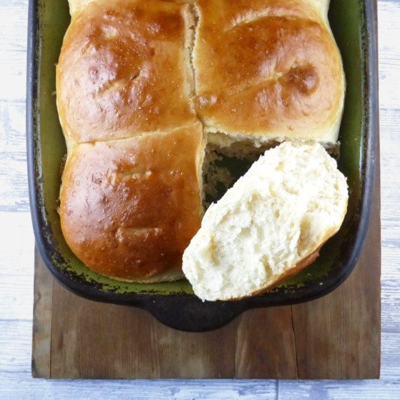 overhead picture of bread buns in a green dish on a wooden plank