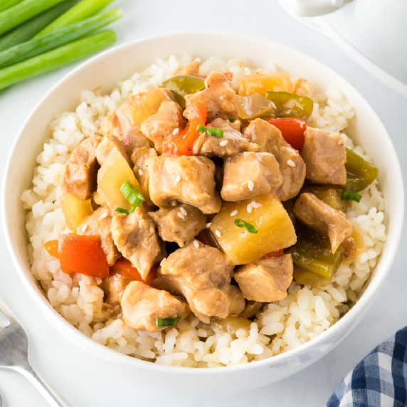 A bowl of rice topped with pork, bell peppers, and pineapple chunks, garnished with green onions.