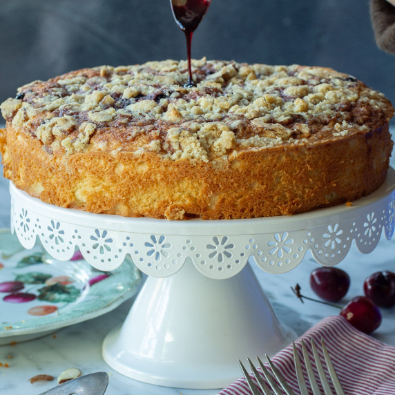 A almond and cherry coffee cake on a white cake pedestal.