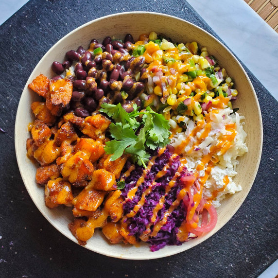 A vibrant bowl of beans, salsa, and sweet potatoes against a black cutting board.