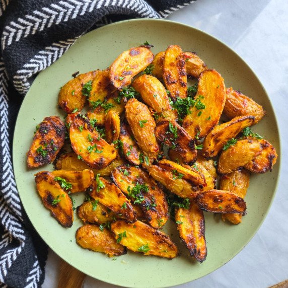 Golden roasted potatoes with green parsley on a green plate.