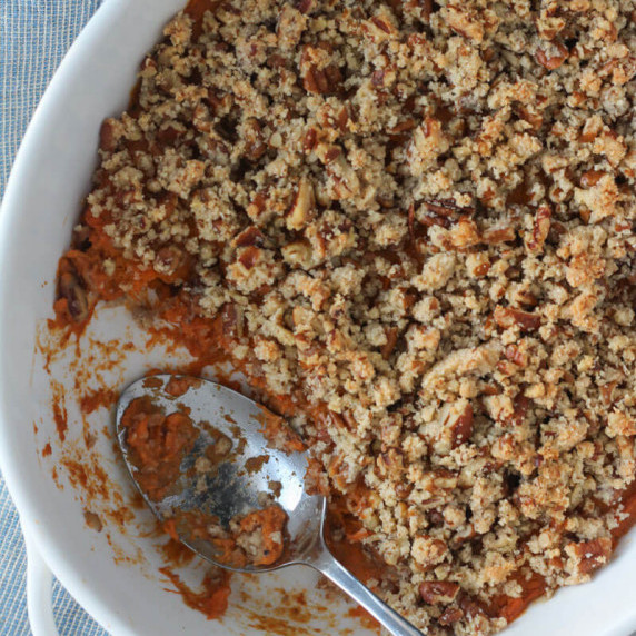 healthy sweet potato casserole with pecan topping in oval white casserole dish with silver spoon