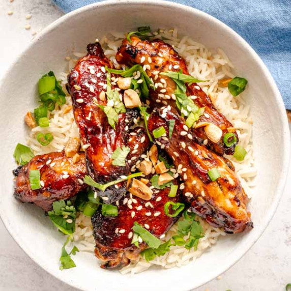 Sticky baked sesame chicken wings sprinkled with sesame seeds over rice on white plate.