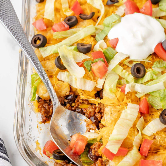 A glass dish with layered taco tater tot casserole.