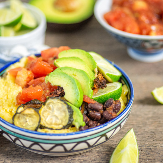 Bowl of creamy polenta topped with roasted vegetables, black beans, salsa, and avocado