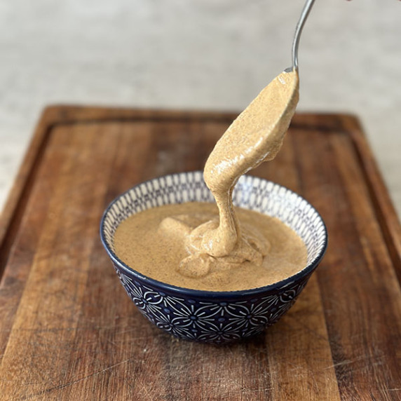 Tandoori mayonnaise in a blue bowl on a wooden board with mayonnaise dripping from a spoon