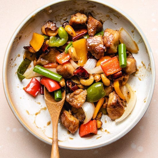 Chicken, red, yellow & green peppers, cashews & onions in a stoneware bowl with wooden spoon