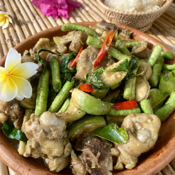 Thai green curry chicken stir-fry in a clay dish with a portion of white rice behind it.
