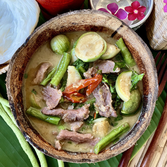 Thai green curry pork with vegetables in a coconut shell.