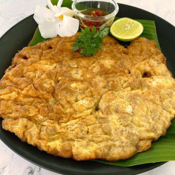 Thai minced pork omelet on a black dish with a wedge of lime, a dip sauce, and coriander.