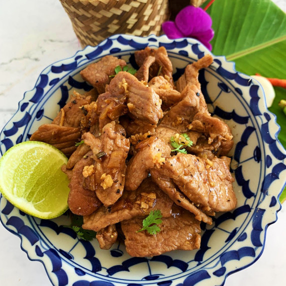 Close-up of Thai pork with garlic and pepper with a wedge of lime in a blue and white bowl.