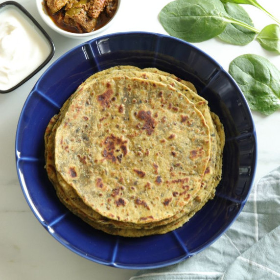 A blue plate with palak methi thepla along with curd and pickle