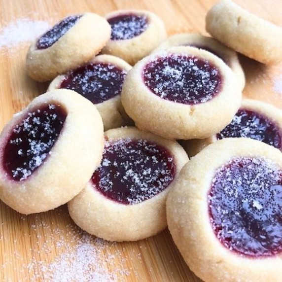 Thumbprint cookies with jam stacked on top of each other on a wooden table. 
