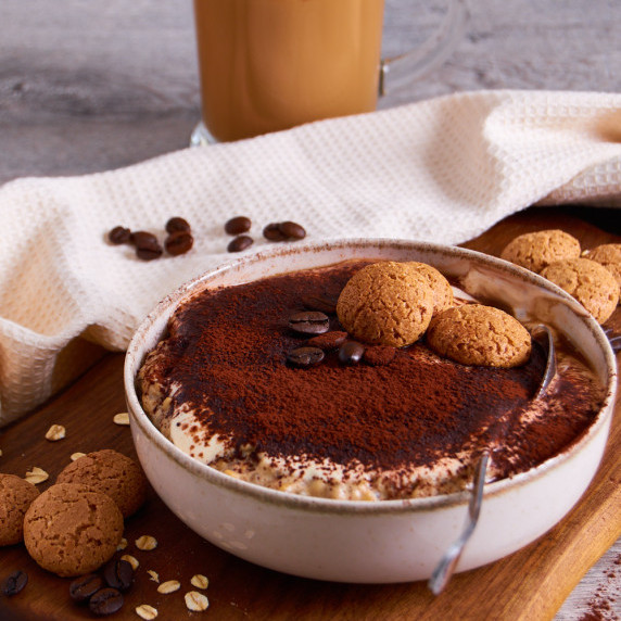A bowl of creamy protein oats topped with cocoa, crunchy amaretti, coffee beans. 