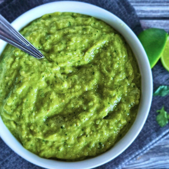 Photo of tomatillo avocado salsa being served in a bowl with a spoon.