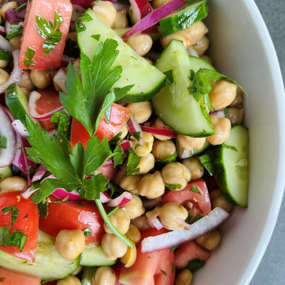 Salad with tomato wedges, cucumber and red onion slices, and chickpeas in a white bowl. 