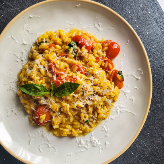 Creamy tomato risotto garnished with pecorino and basil on a gold trimmed white plate.