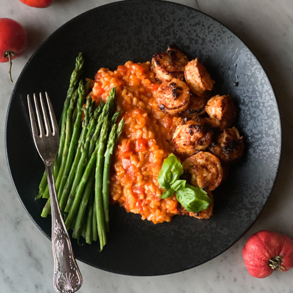 Tomato risotto on a plate with shrimp and basil, and asparagus and a fork.