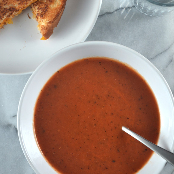 Tomato soup in a white bowl and cheese toasty on plate on marble countertop