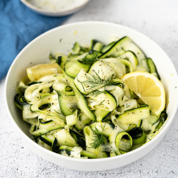 shaved zucchini ribbon salad with wedges of lemon and dill fronds in a white bowl.
