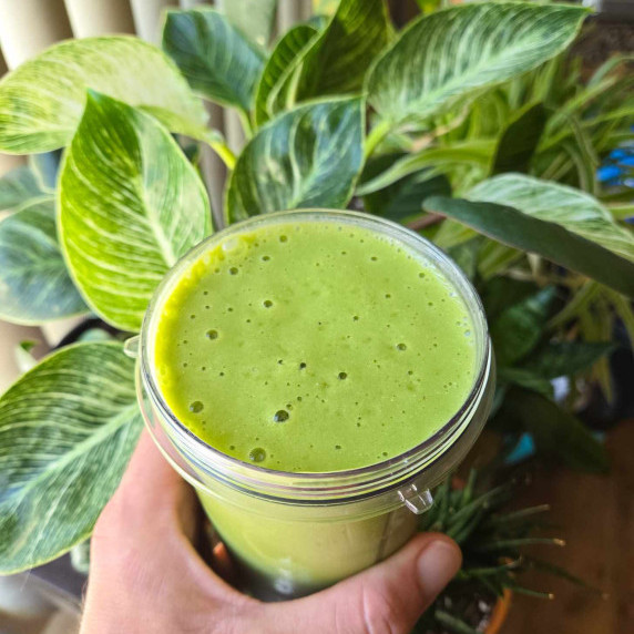 A bright green smoothie surrounded by green plants.