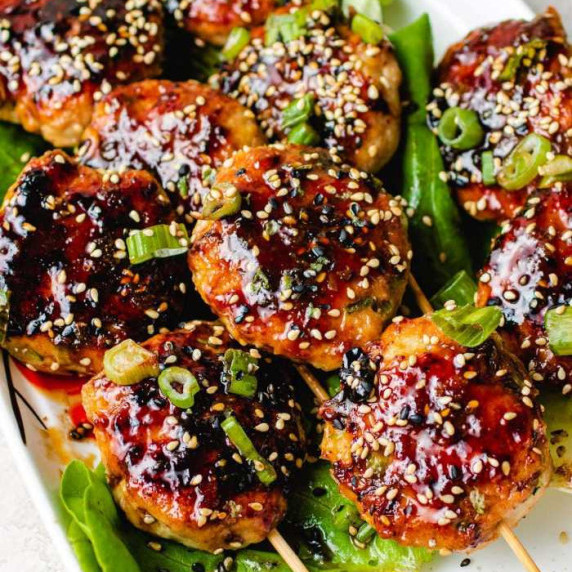 Grilled meatballs on skewers with sauce and sesame seeds on a bed of lettuce