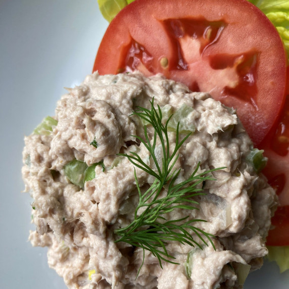 Tuna salad mounded on top of tomato slices and leaf lettuce.