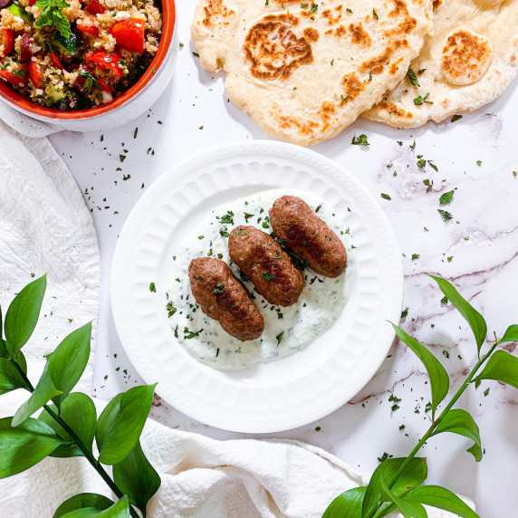turkey kofta on a plate of tzatziki with a warm pitas and salad on a white marble counter
