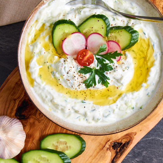 A bowl of creamy Easy Tzatziki garnished with cucumber, tomato, and radishes. 
