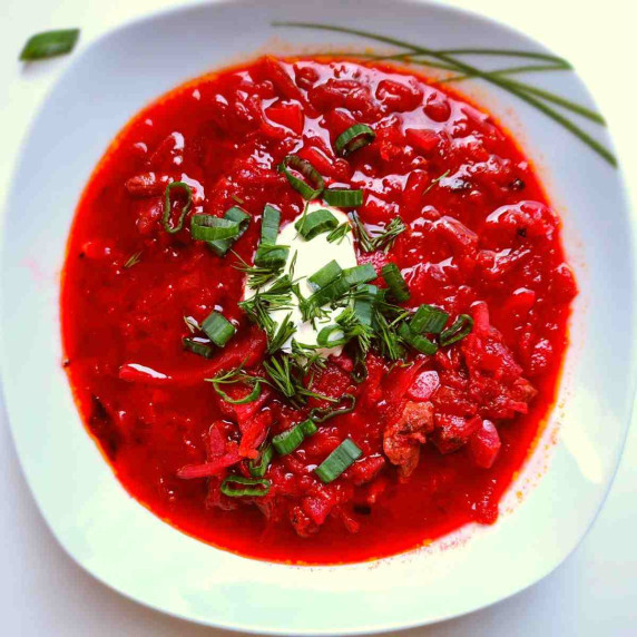A white plate with red borscht and greens on top.