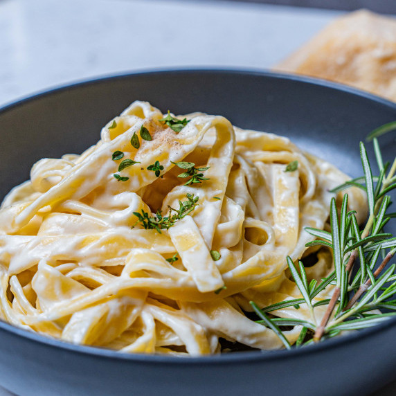Fettuccine alfredo pasta coated with alfredo sauce with thyme leaves and rosemary