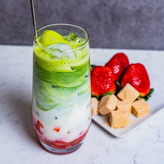 Strawberry matcha latte in a tall glass with strawberries and and wafer cookies