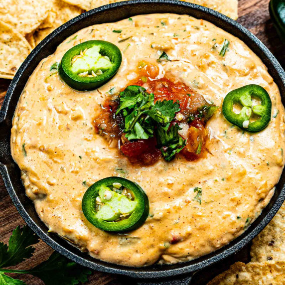 Salsa Con Queso in a cast iron skillet garnished with salsa and jalapenos
