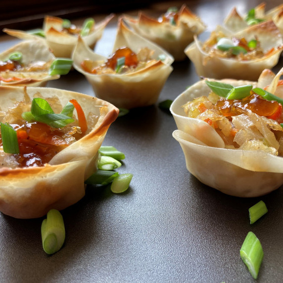 Egg roll filling in wonton wrappers topped with scallion slices on a black plate.