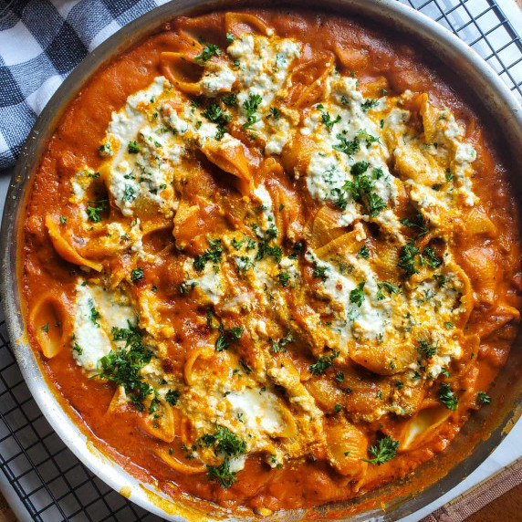 A skillet full of tomatoey pasta and white dollops of creamy ricotta.