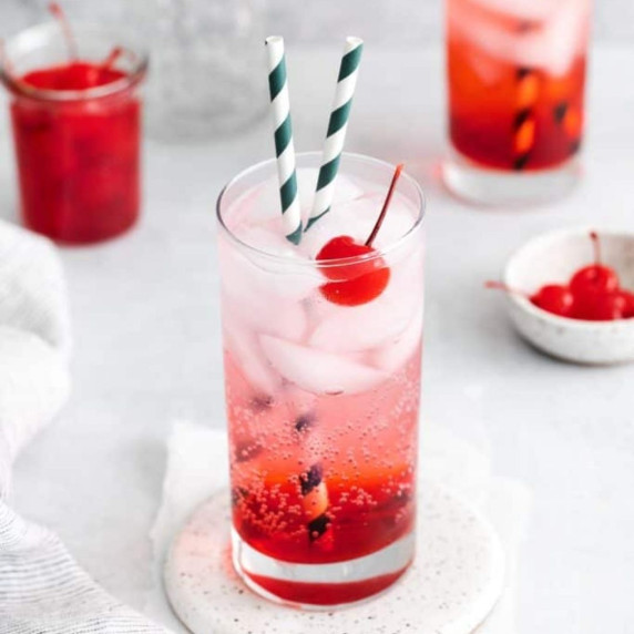 Glass of iced shirley temple with two straws and a cherry garnish on a coaster