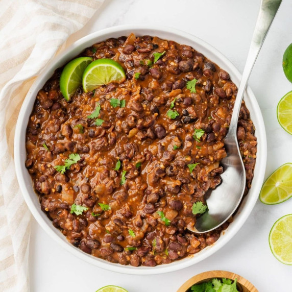 Black beans garnished with chopped cilantro and two lime slices in a white bowl with a silver spoon 