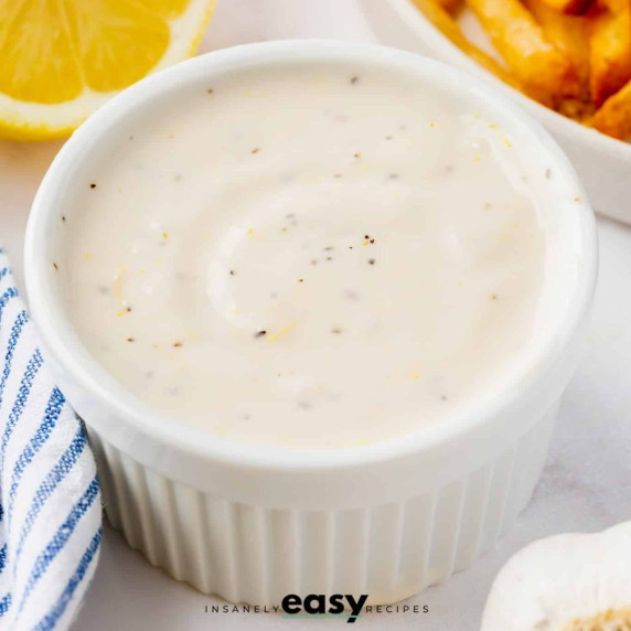 Lemon garlic aioli in a white cup served with french fries, a lemon slice at the back