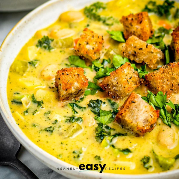 White bean and kale soup topped with croutons and chopped parsley in a white bowl 