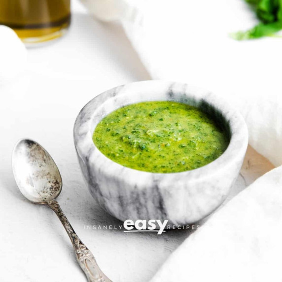 Basil pesto in a marble bowl and a spoon next to it on a white countertop