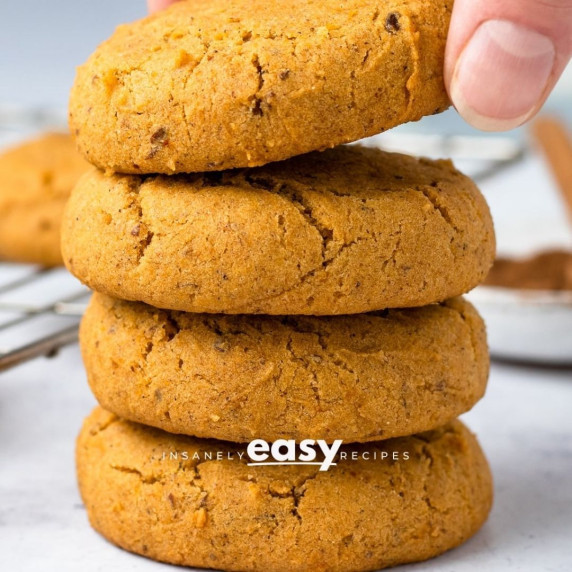 Four stacked vegan pumpkin cookies on a white surface