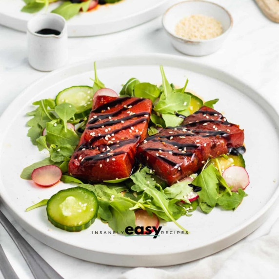 Watermelon steaks topped with balsamic glaze drizzled and sesame seeds on a white plate