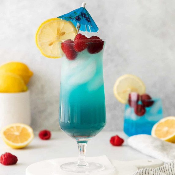 Iced blue grateful dead cocktail in a tall glass served with raspberries and a lemon wheel