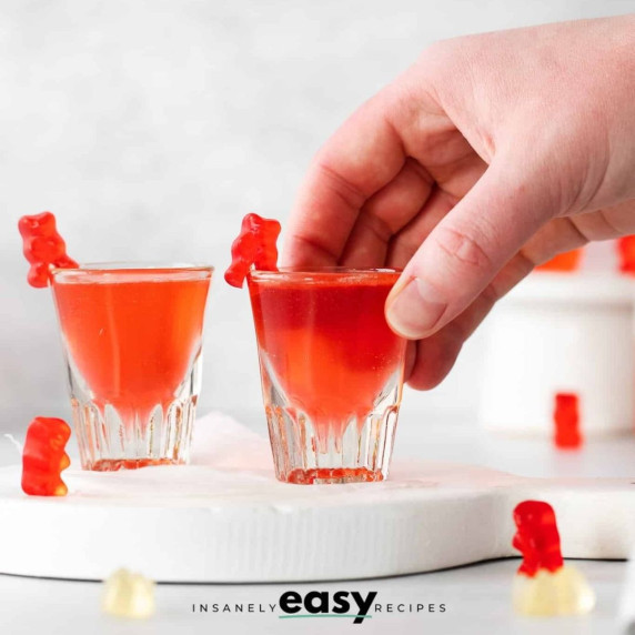 Two red-colored shots in shot glasses with red gummy bears on the rim