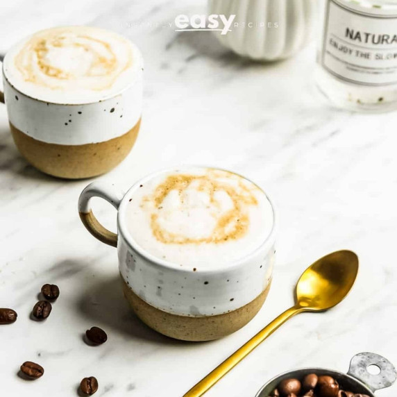 Oat milk latte in two cups sprinkled with some cinnamon powder on top, few coffee beans on the side