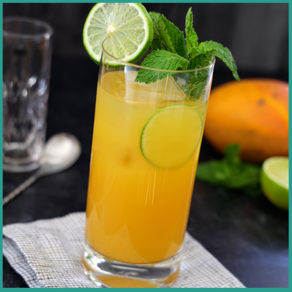 Tall glass with mango mojito garnished with fresh mint and lime slices.