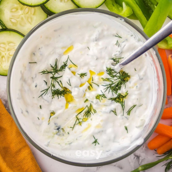 Mediterranean sauce topped with dill and olive oil in a bowl with sliced fruits around