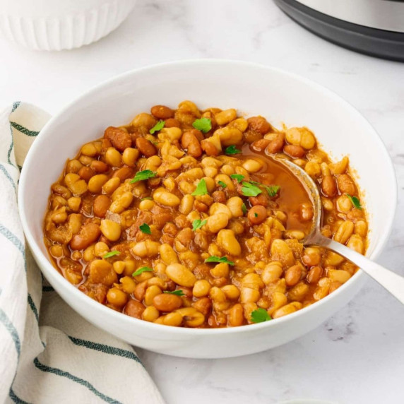 Baked beans garnished with chopped green herbs in a white bowl with a spoon